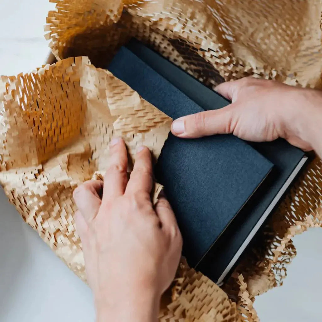 Hands packing black notebooks in eco-friendly packaging material